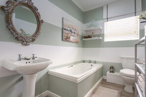 A bathroom with a pedestal sink, a freestanding bathtub, a toilet, and a decorative mirror.