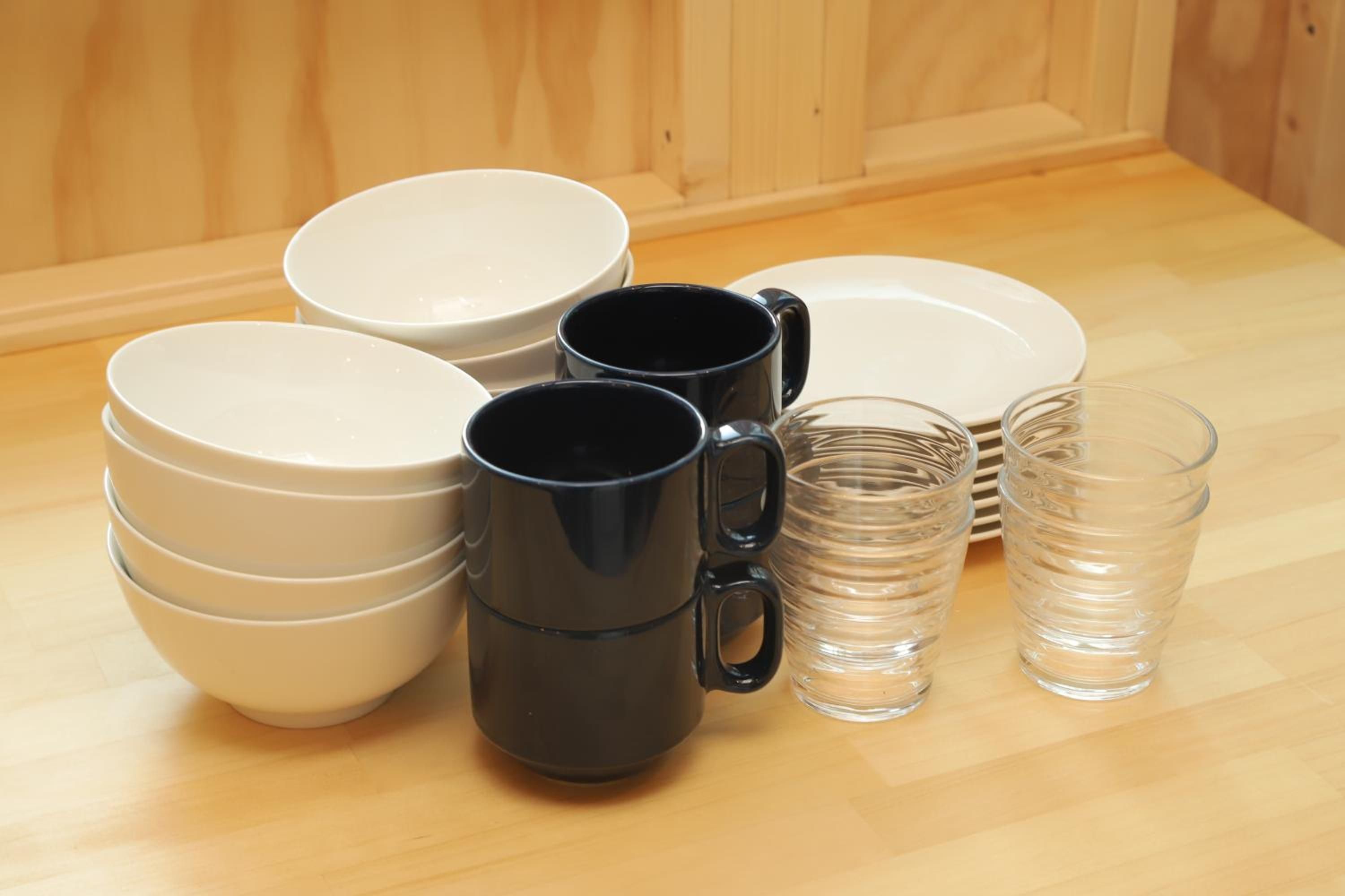 A set of white bowls, black mugs, and clear glasses arranged on a wooden surface.