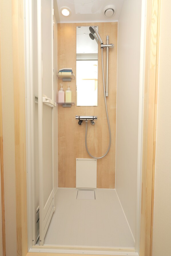 Une petite cabine de douche avec un mur en panneaux de bois, un pommeau de douche à main, un robinet mural et une petite étagère contenant des articles de toilette.