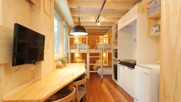 A compact wooden cabin with bunk beds, a dining area with chairs, a television, and a refrigerator. - JR Mobile Inn Sapporo Kotoni (Sapporo)