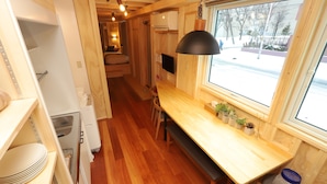 A compact kitchen with wooden cabinets, a dining table, and a window overlooking a snowy street. - JR Mobile Inn Sapporo Kotoni (Sapporo)