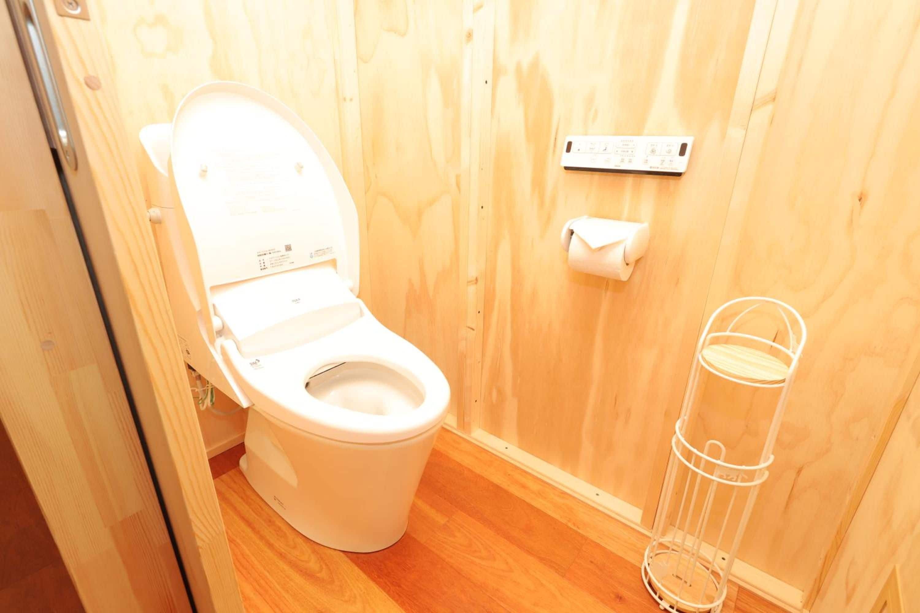 Un baño pequeño y funcional con inodoro blanco, piso de madera y un sujetador de papel higiénico blanco en la pared.