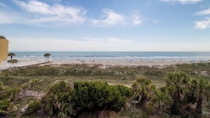 A beach with a clear sky, a sandy shore, and some greenery in the foreground. - 3BR/3BA Oceanview just steps from the sand~ 107 Ocean Pointe (Folly Beach)