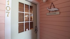 A door with the number 107, a window with blinds, a 'WELCOME' sign, and a wall-mounted light fixture. - 3BR/3BA Oceanview just steps from the sand~ 107 Ocean Pointe (Folly Beach)
