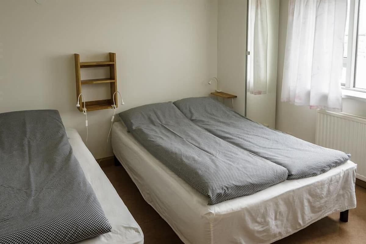 A bedroom with two single beds, a wooden shelf, a bedside table, and a window with curtains.