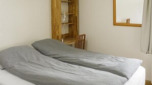 Een enkel bed met een gestreept dekbedovertrek, een houten bureau met een stoel, en een spiegel aan de muur.