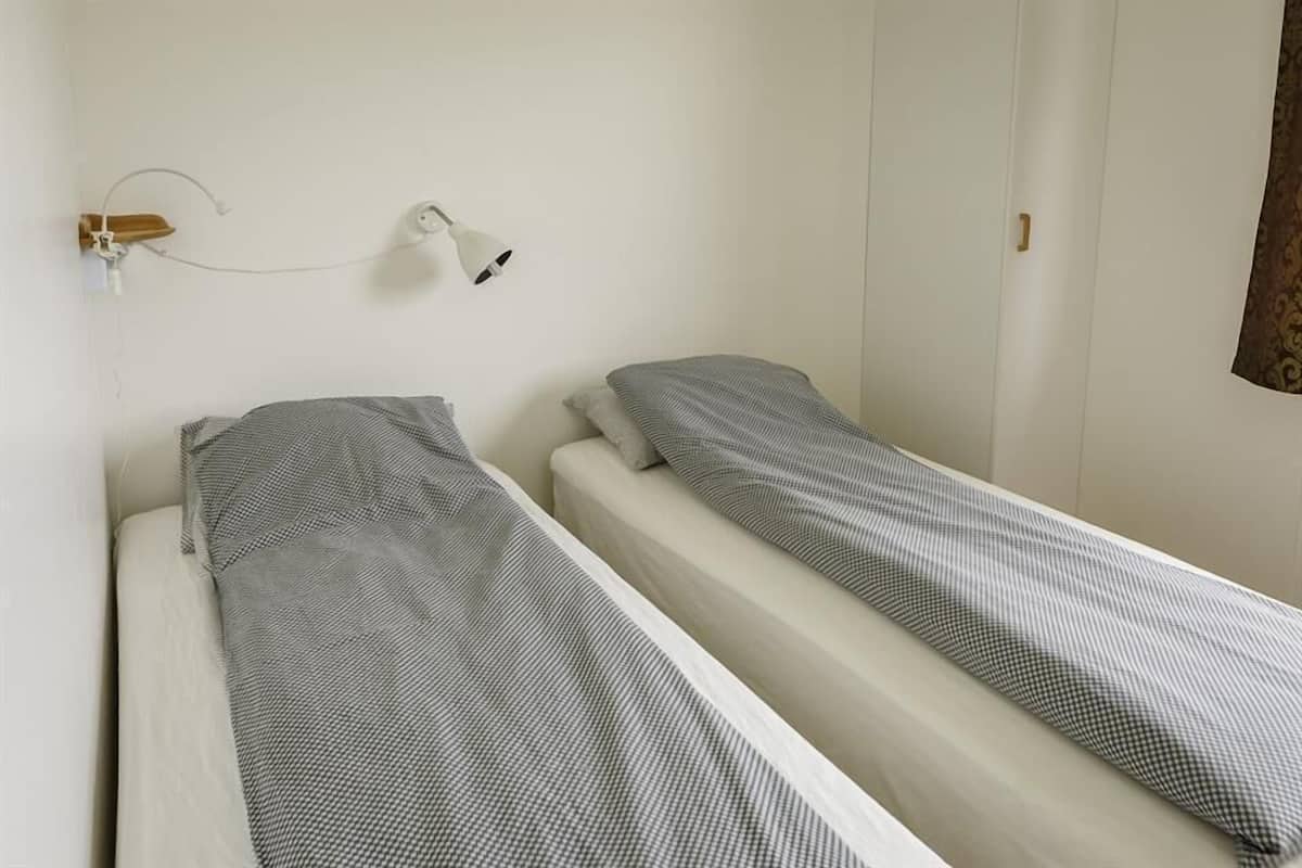 A simple, clean room with two single beds, a wall-mounted lamp, and a wardrobe.