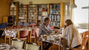 Een knusse bibliotheek met boekenkasten, een eetgedeelte met tafels met tafellinnen en een raam dat natuurlijk licht binnenlaat.
