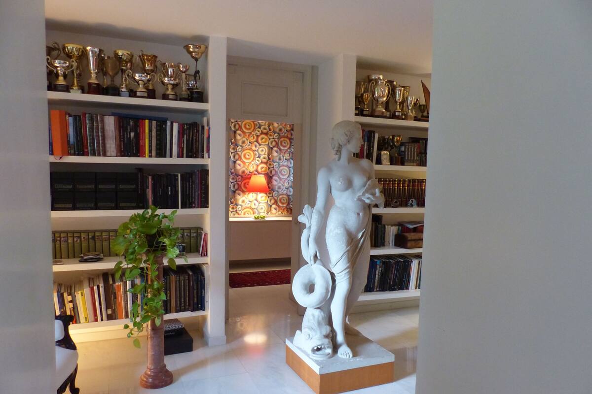 A room with a statue, bookshelves, and a lamp.