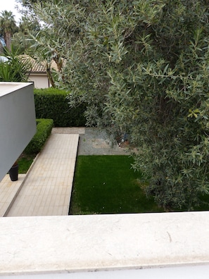 Un espace extérieur moderne avec un chemin pavé, des haies soigneusement taillées et une petite pelouse.