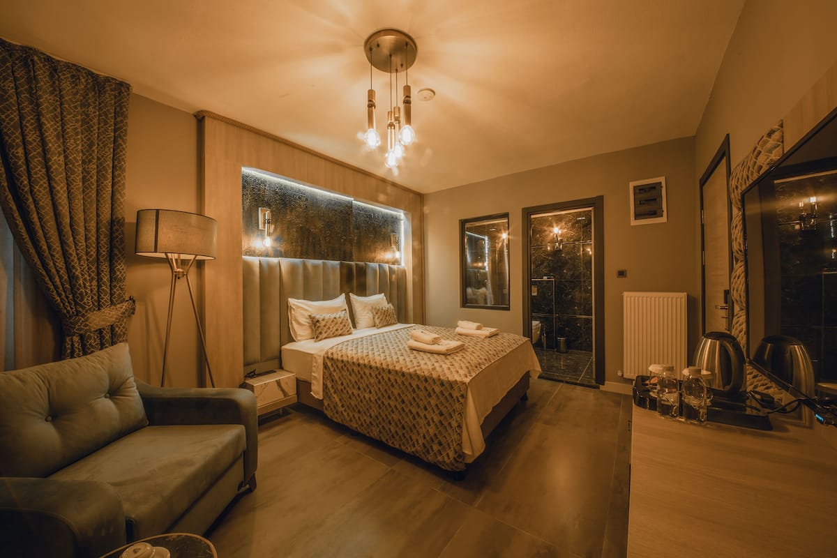 A modern bedroom with a large bed, a sofa, a desk, and a view of the outdoors.