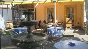 Un patio al aire libre con una fuente de piedra, mesas redondas con manteles azules y sillas de mimbre.