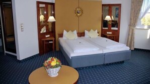 Habitación de hotel con cama doble, dos mesitas de noche con lámparas, un espejo grande y una pequeña mesa redonda con un arreglo floral.