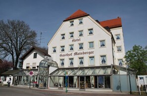 Een hotel met een groot bord waarop 'Hotel Gasthof Maisberger' staat, op een wit gebouw met meerdere ramen.