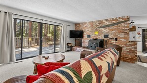 Ein gemütliches Wohnzimmer mit Kamin, großem Fernseher und einer Schiebetür zu einer Terrasse.