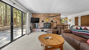 Ein Wohnzimmer mit Backsteinwand, Kamin, einer Ledersofa und einem großen Fenster mit Blick auf einen Wald.