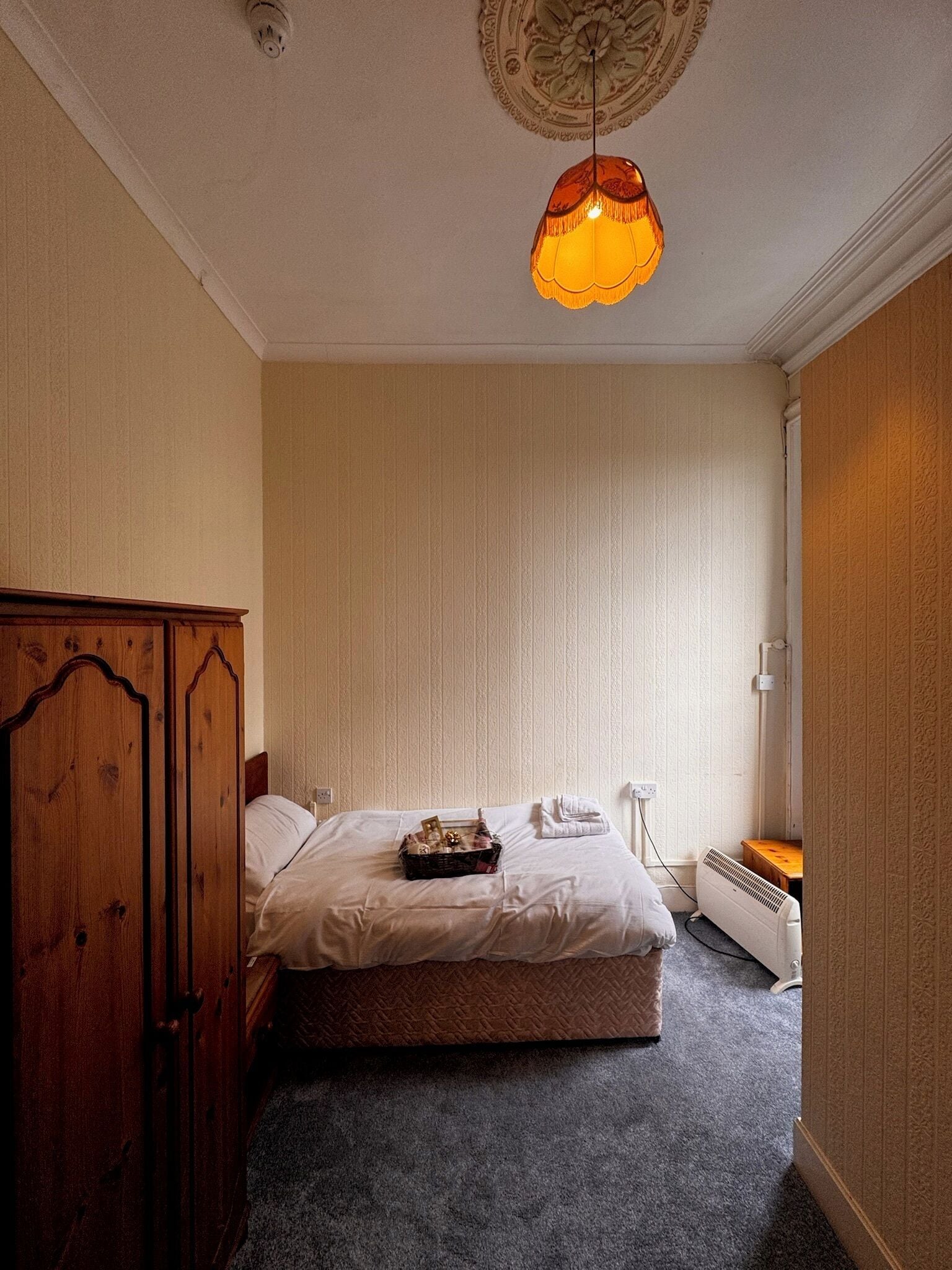 Ein Schlafzimmer mit Bett, Holzschrank, Nachttisch, Heizung und einer Pendelleuchte.