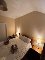 Un dormitorio con una cama, mesitas de noche, una lámpara y una cesta sobre la cama.