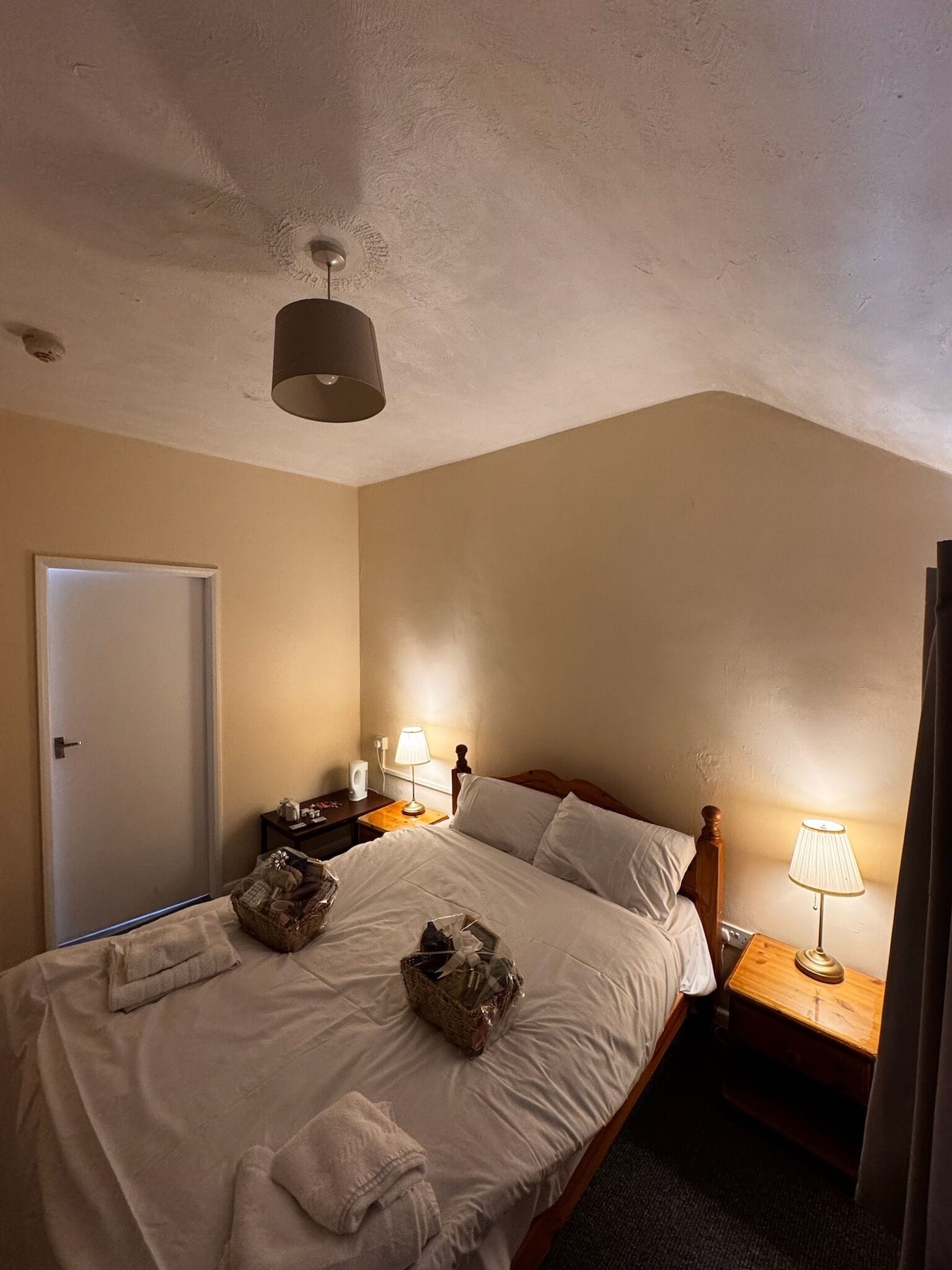 Une chambre d’hôtel avec un lit, des tables de chevet, une lampe, une porte et un luminaire au plafond.