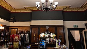 A bar area with a chandelier, bar stools, and a clock on the wall. - Pinegrove Hotel (Carlisle)