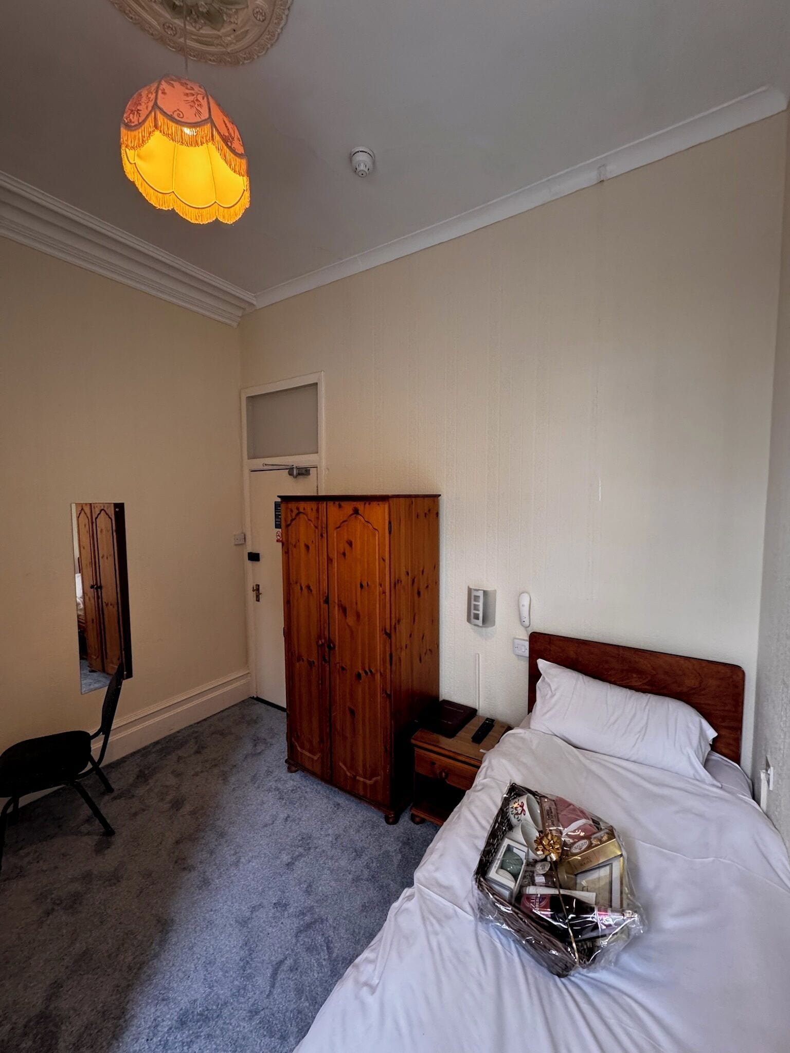 Una habitación de hotel con cama, armario de madera, escritorio, silla, lámpara colgante e iluminación de techo.