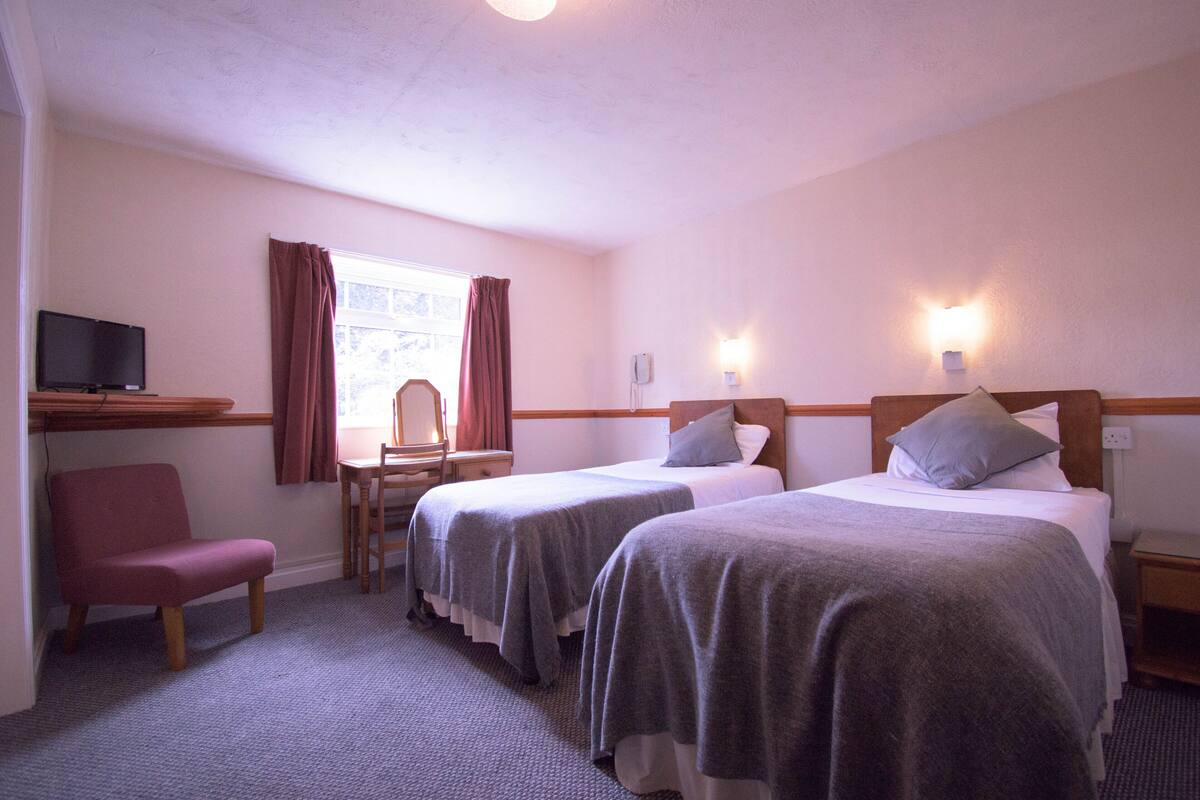 Quarto de hotel com duas camas, uma escrivaninha, uma cadeira e uma televisão.