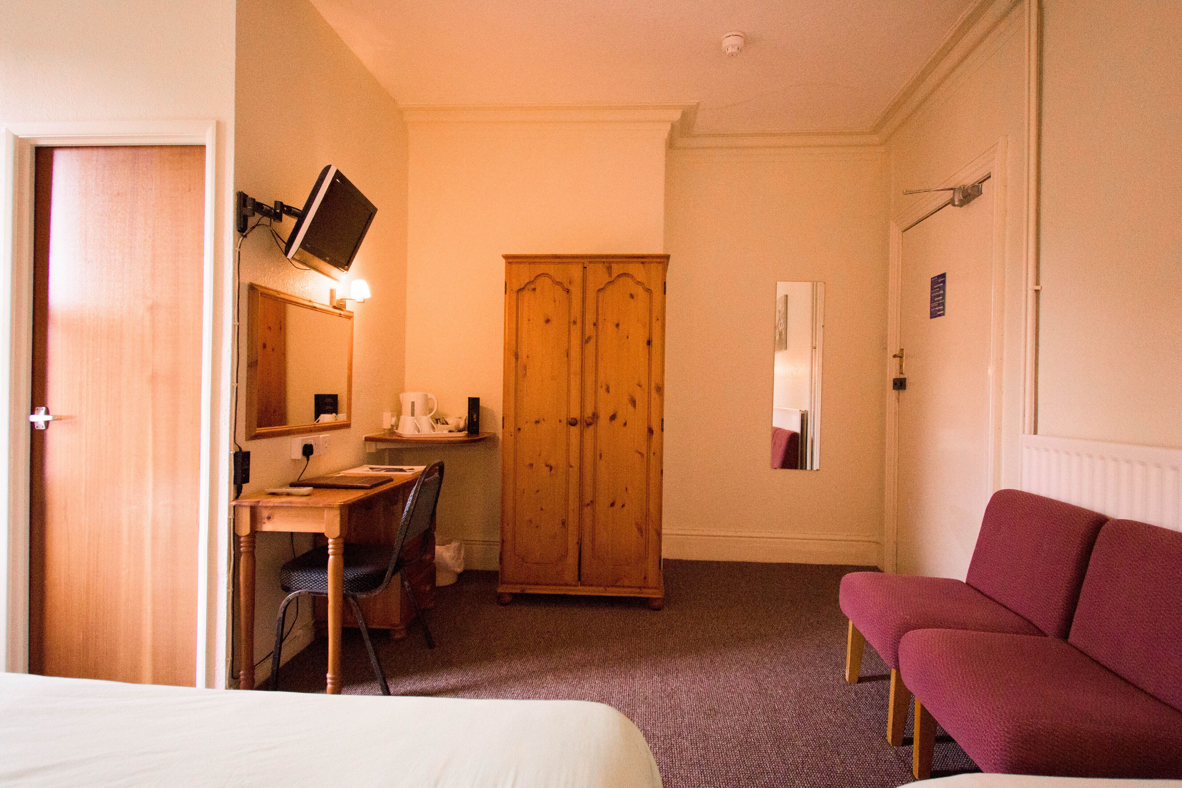 A hotel room with a bed, a desk with a chair, a wardrobe, and a red sofa.