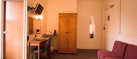 A hotel room with a bed, a desk with a chair, a wardrobe, and a red sofa.
