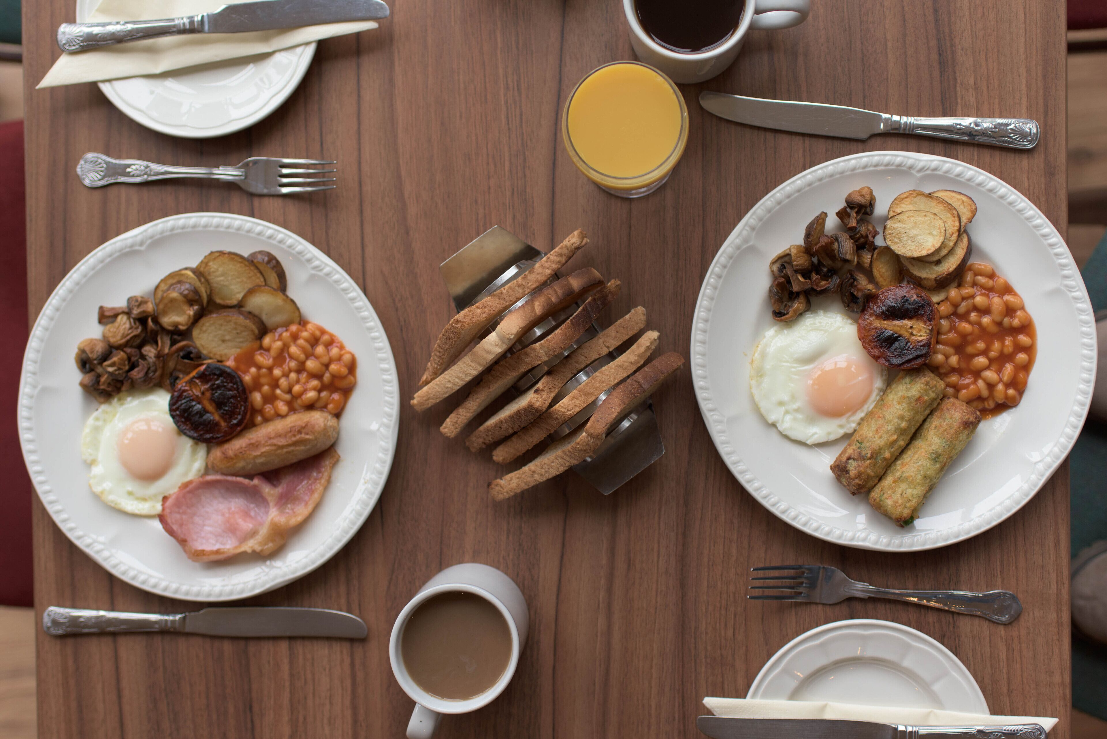 A breakfast setting with two plates of eggs, sausages, beans, and toast.
