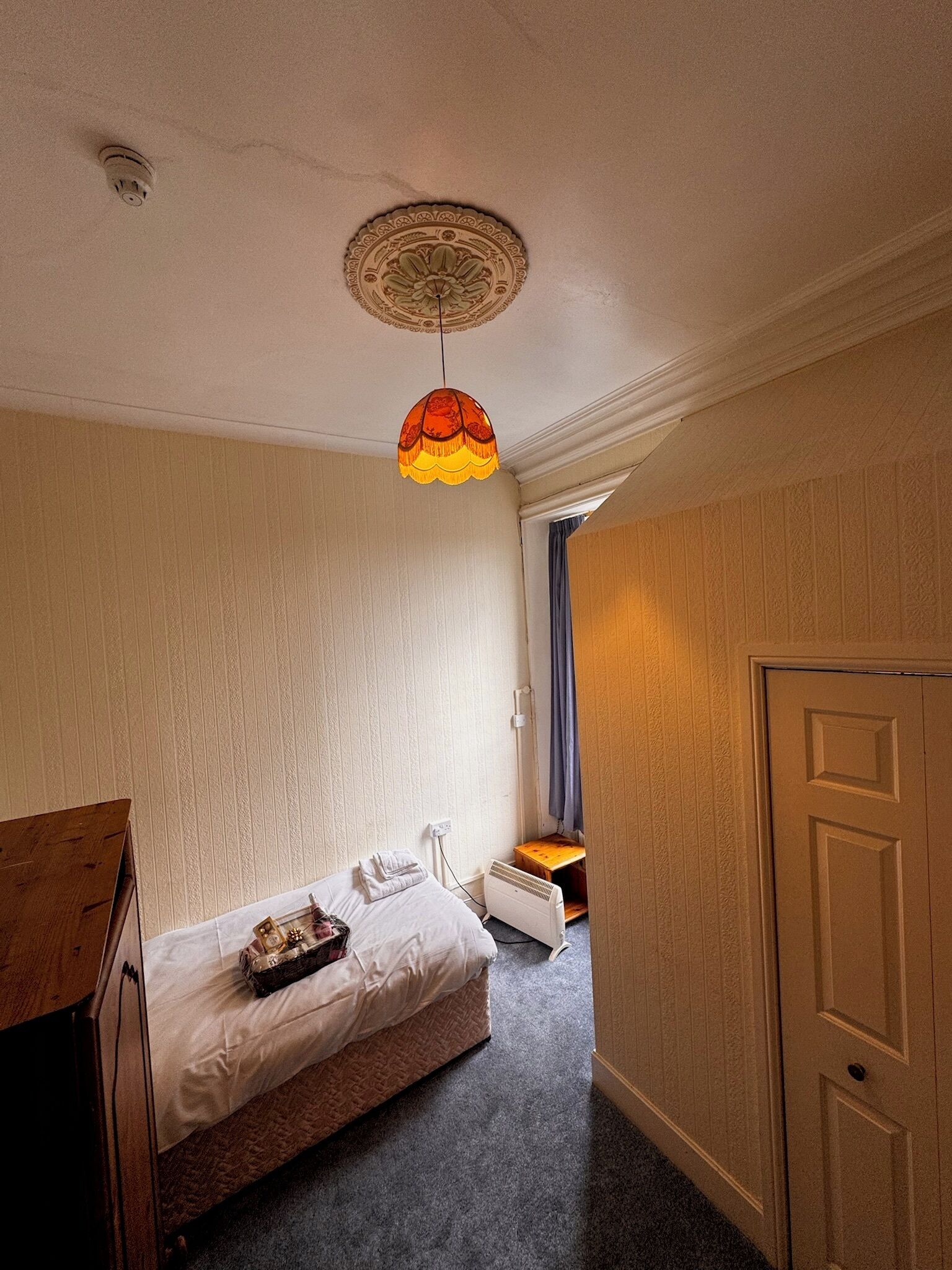 A bedroom with a bed, a wooden dresser, a heater, and a door.