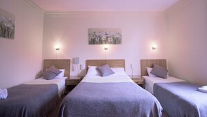 A hotel room with three single beds, each with a pillow and a blanket. There are bedside tables with lamps and a phone on one side. - Pinegrove Hotel (Carlisle)