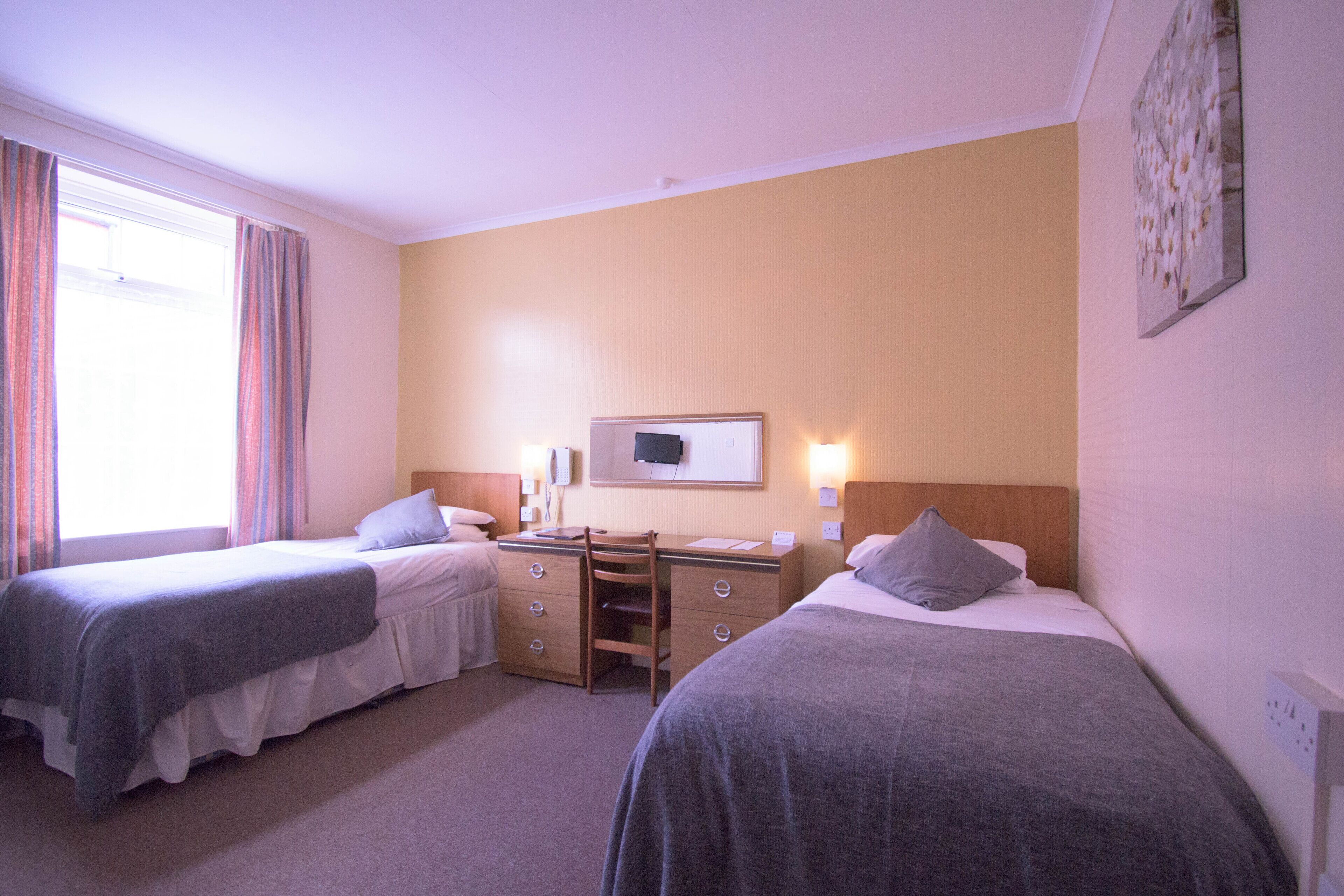 A hotel room with two beds, a desk, and a television.
