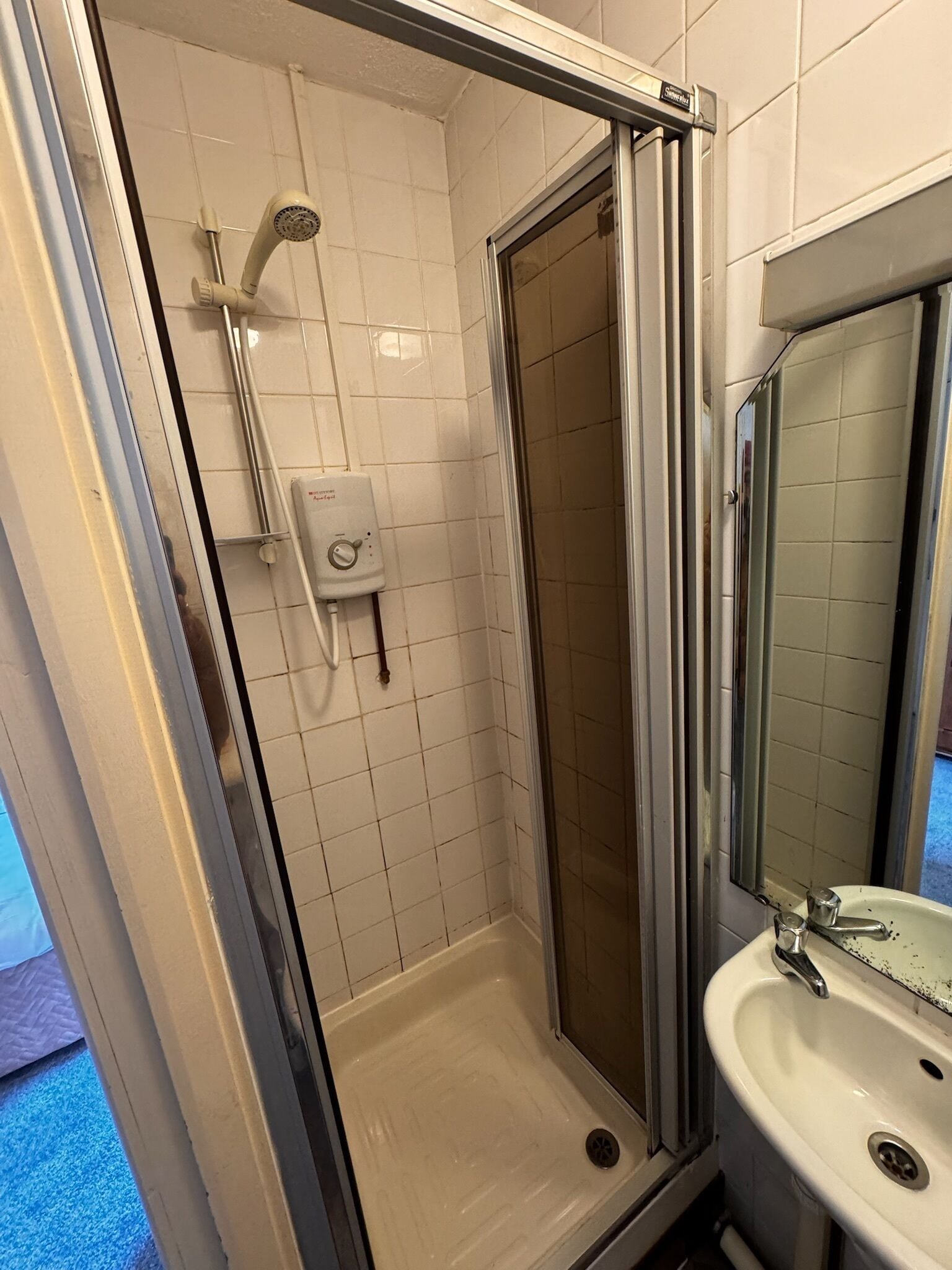 A shower with a handheld showerhead, a handheld water pump, and a glass door.