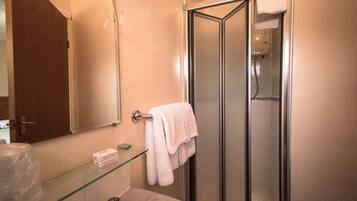 Un baño con cabina de ducha de vidrio, un lavamanos blanco y un estante de vidrio con una caja.