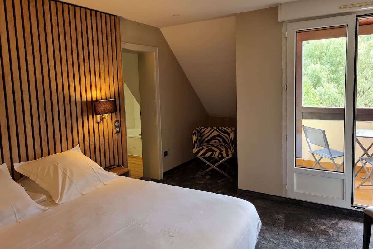 A bedroom with a bed, a wooden slat wall, a chair, and a balcony with a table and chairs.