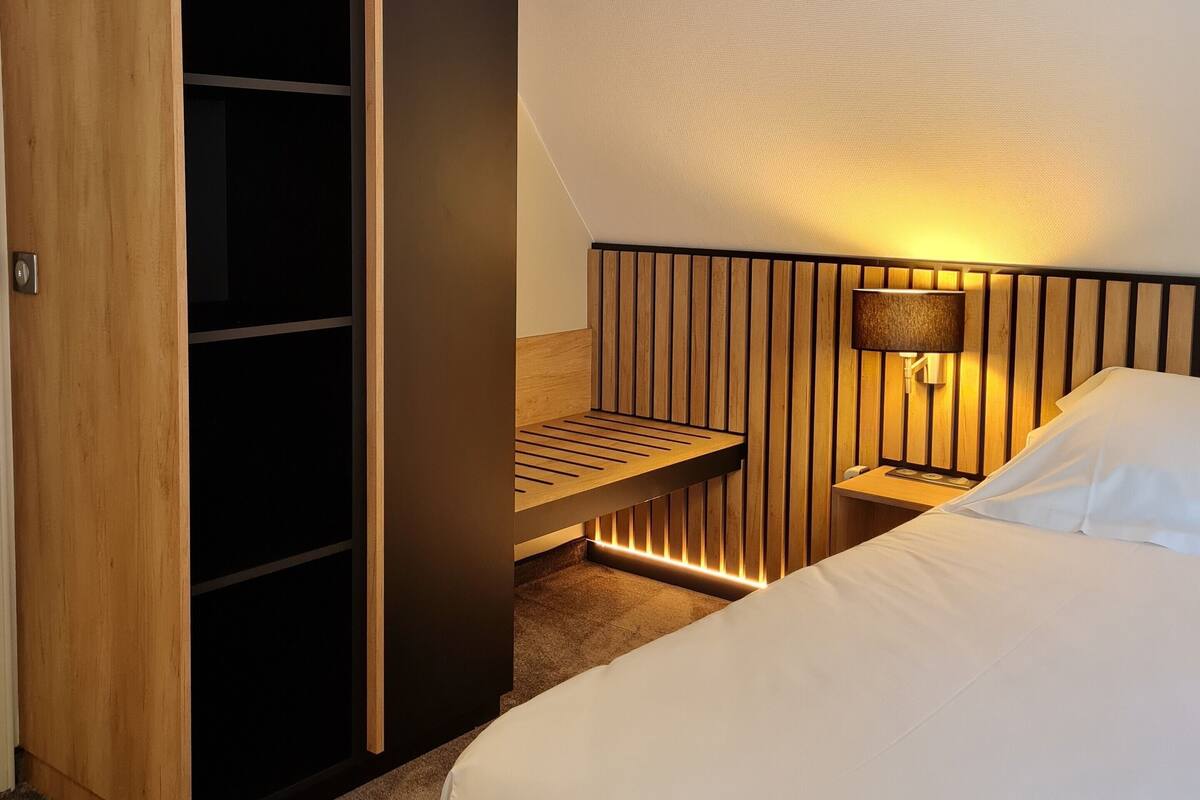 A bedroom with a bed, a wooden wardrobe, a bedside table with a lamp, and a headboard with vertical wooden slats.