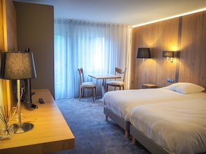 A hotel room with a bed, a desk with a lamp, a chair, a small table, and a window with curtains. - La Couronne by K (Reipertswiller)