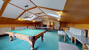 Una habitación amplia con mesa de billar, sofá y mesa de ping pong.