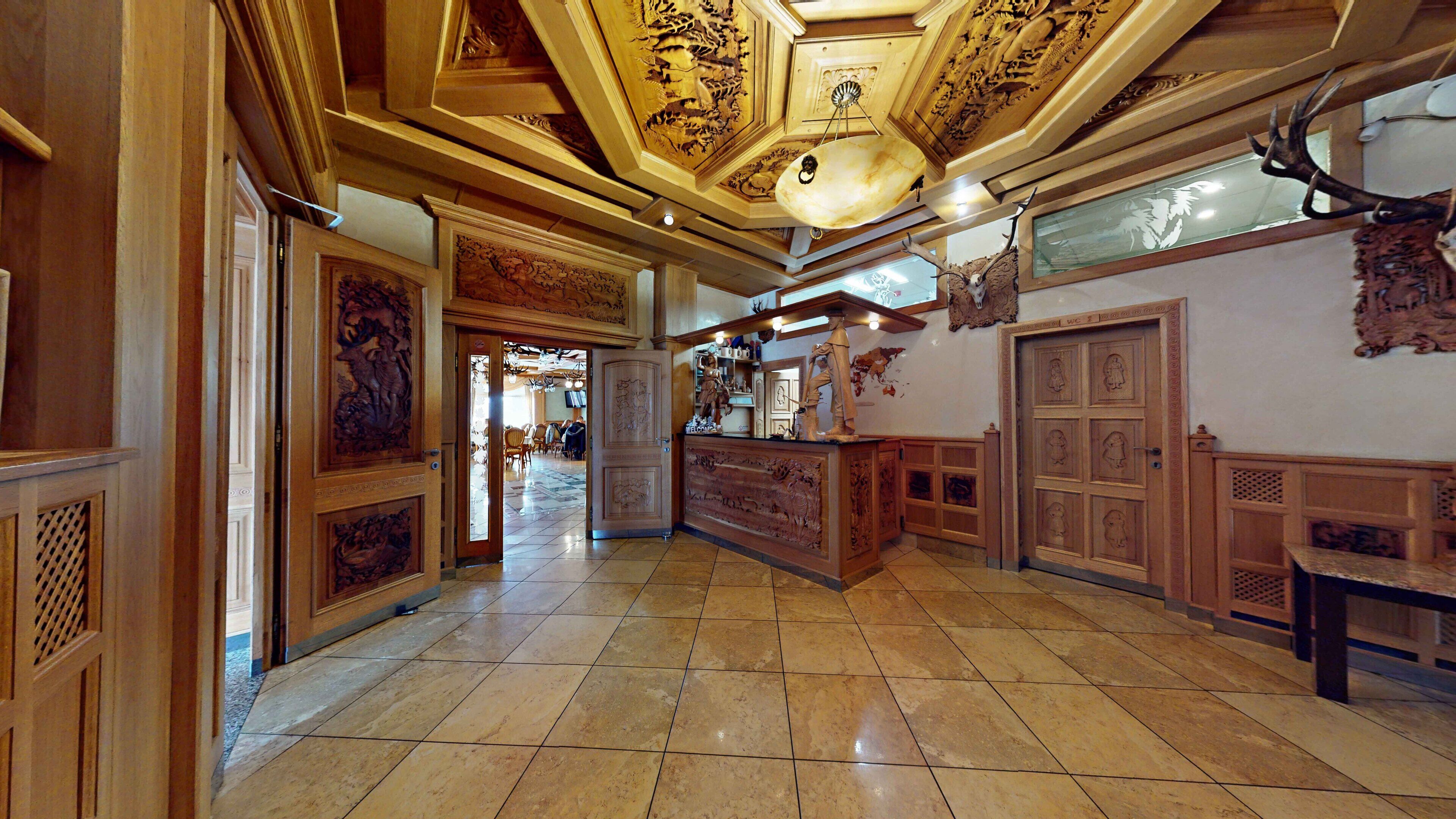 Eine Hotelhalle mit aufwendiger Holzvertäfelung, Fliesenboden und einer Decke mit kunstvollen Schnitzereien.