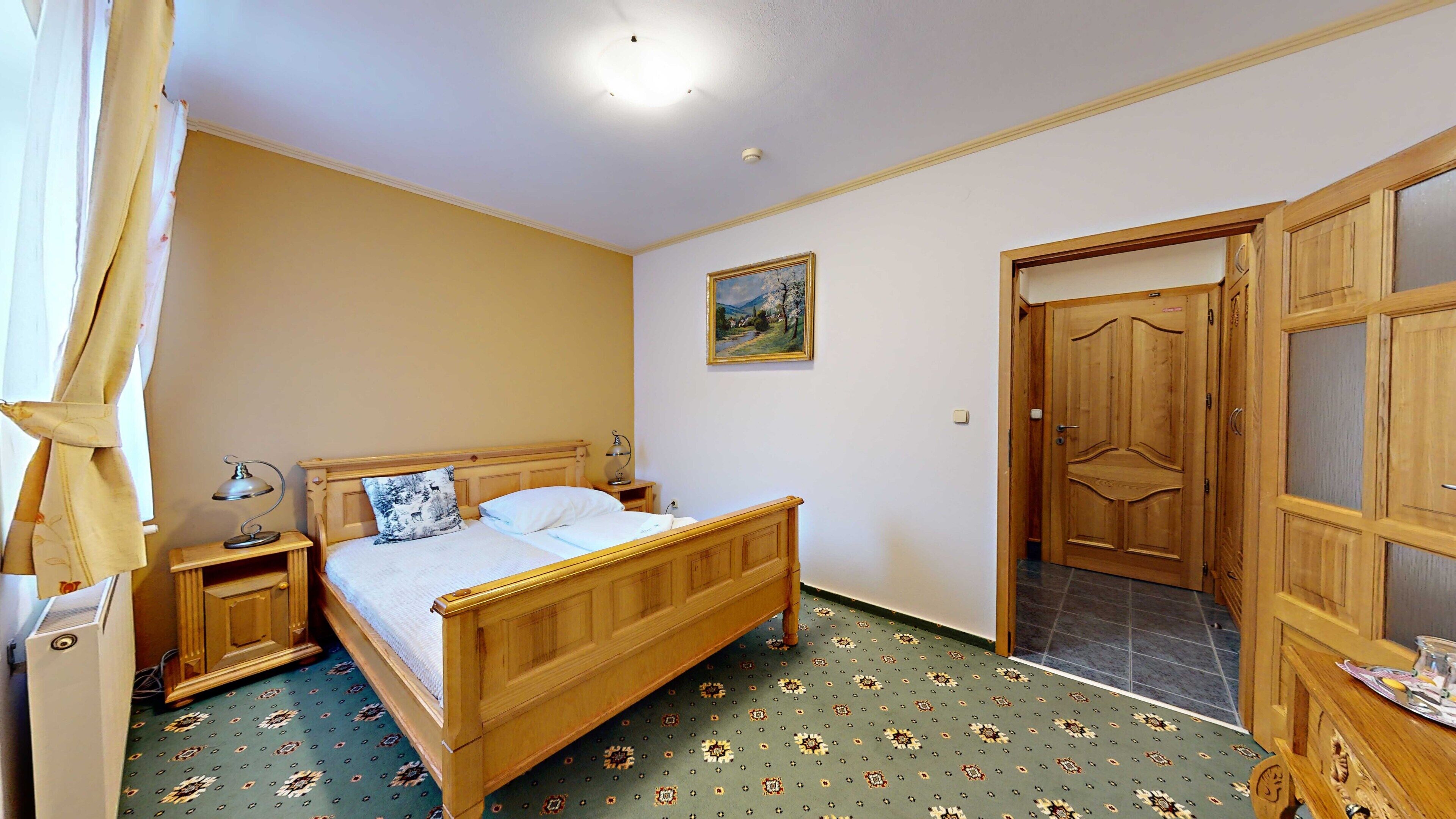 Une chambre à coucher avec un lit en bois, une table de chevet avec une lampe, un tableau au mur et une armoire à porte vitrée.