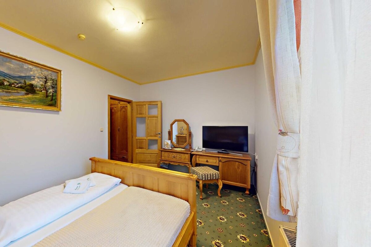 A hotel room with a bed, a desk with a television, a wardrobe, and a painting on the wall.