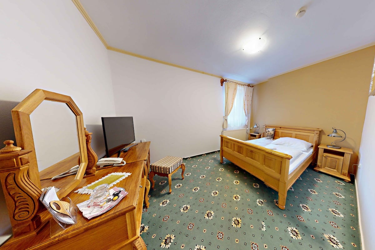 Une chambre à coucher avec un lit en bois, un bureau avec un ordinateur, un miroir et une commode.