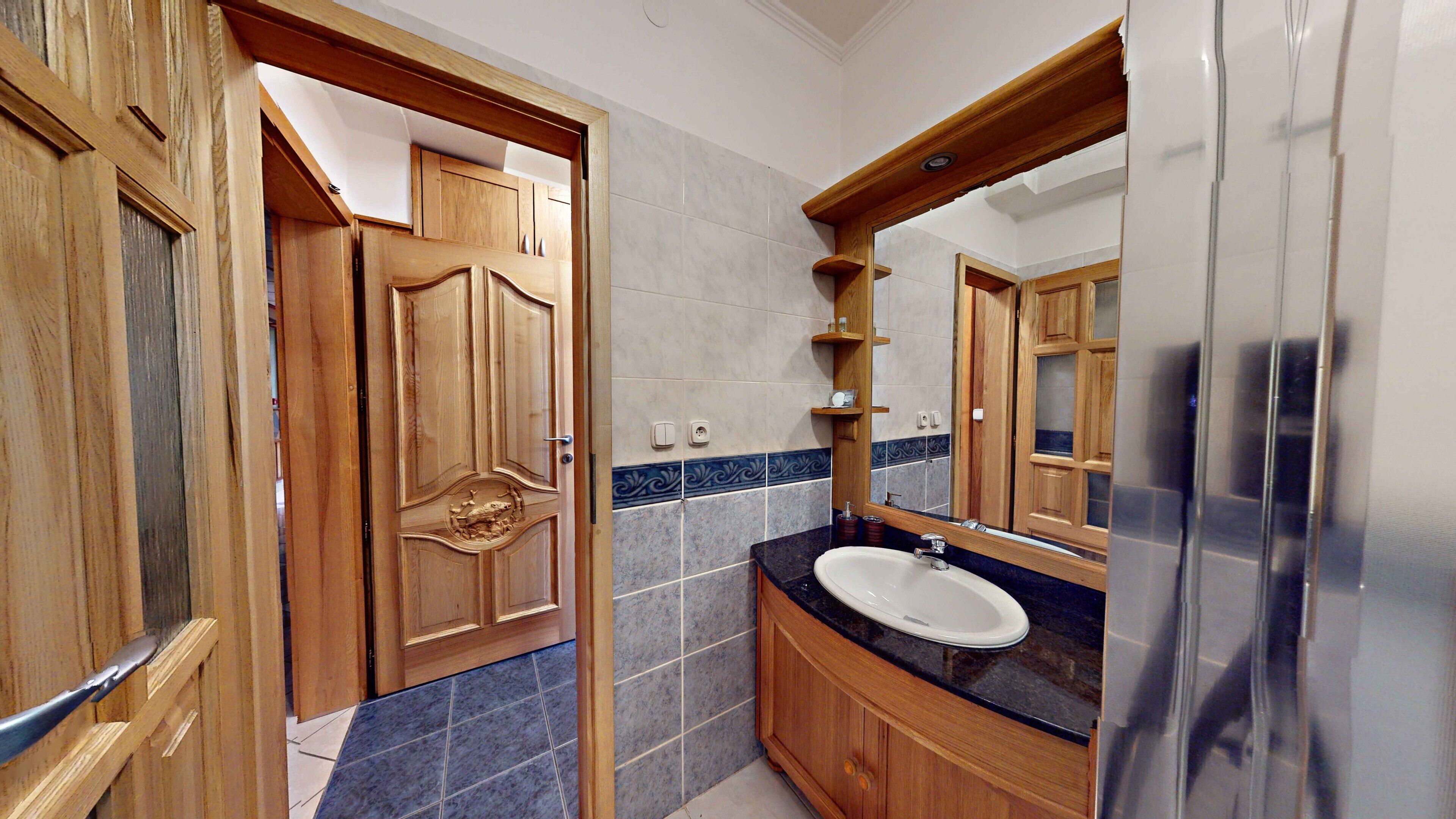 A bathroom with wooden cabinets, a marble-tiled wall, a sink, and a mirror.