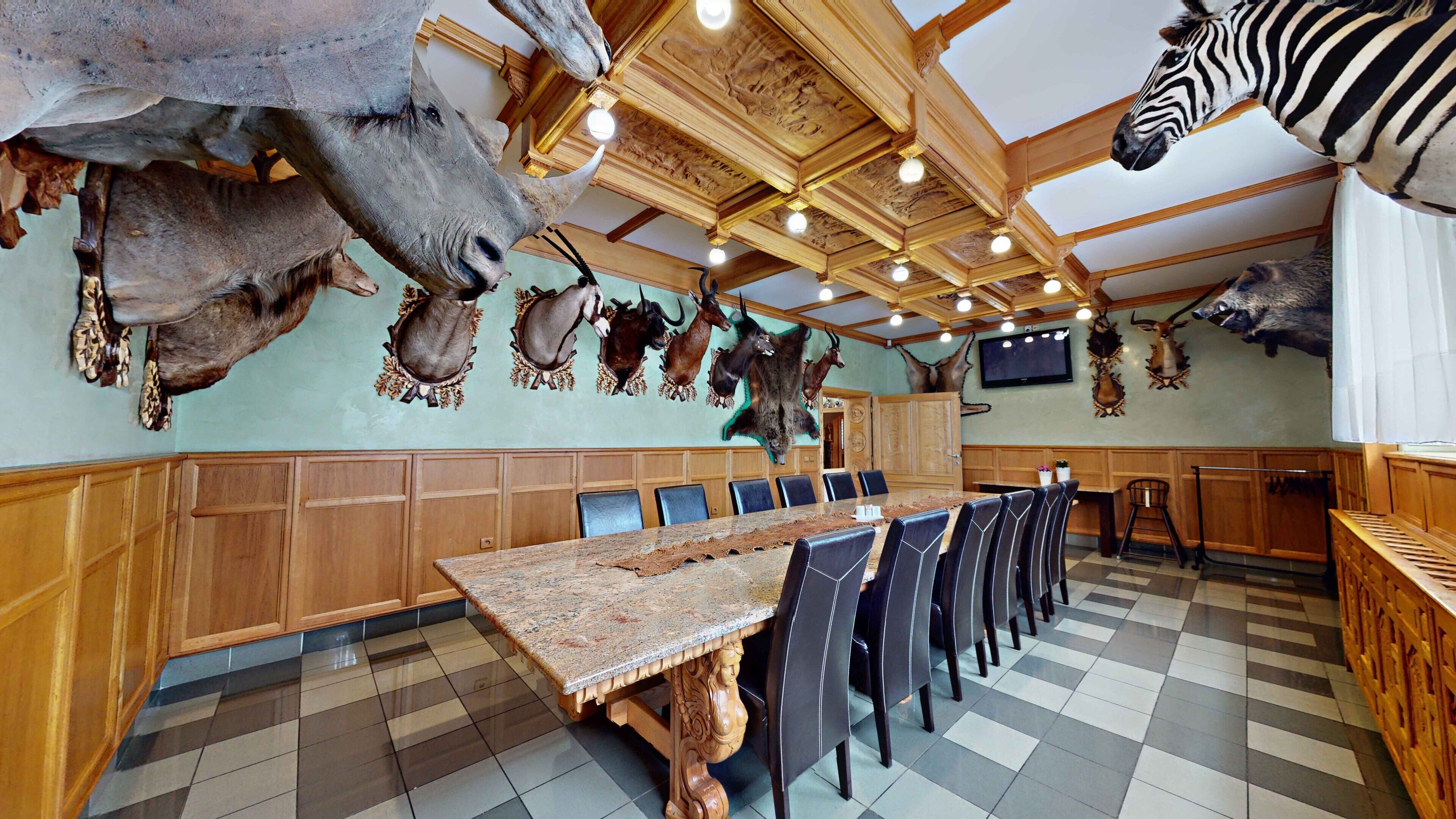 A restaurant with a long wooden table and chairs, a high ceiling with wooden beams, and walls decorated with mounted animal heads.