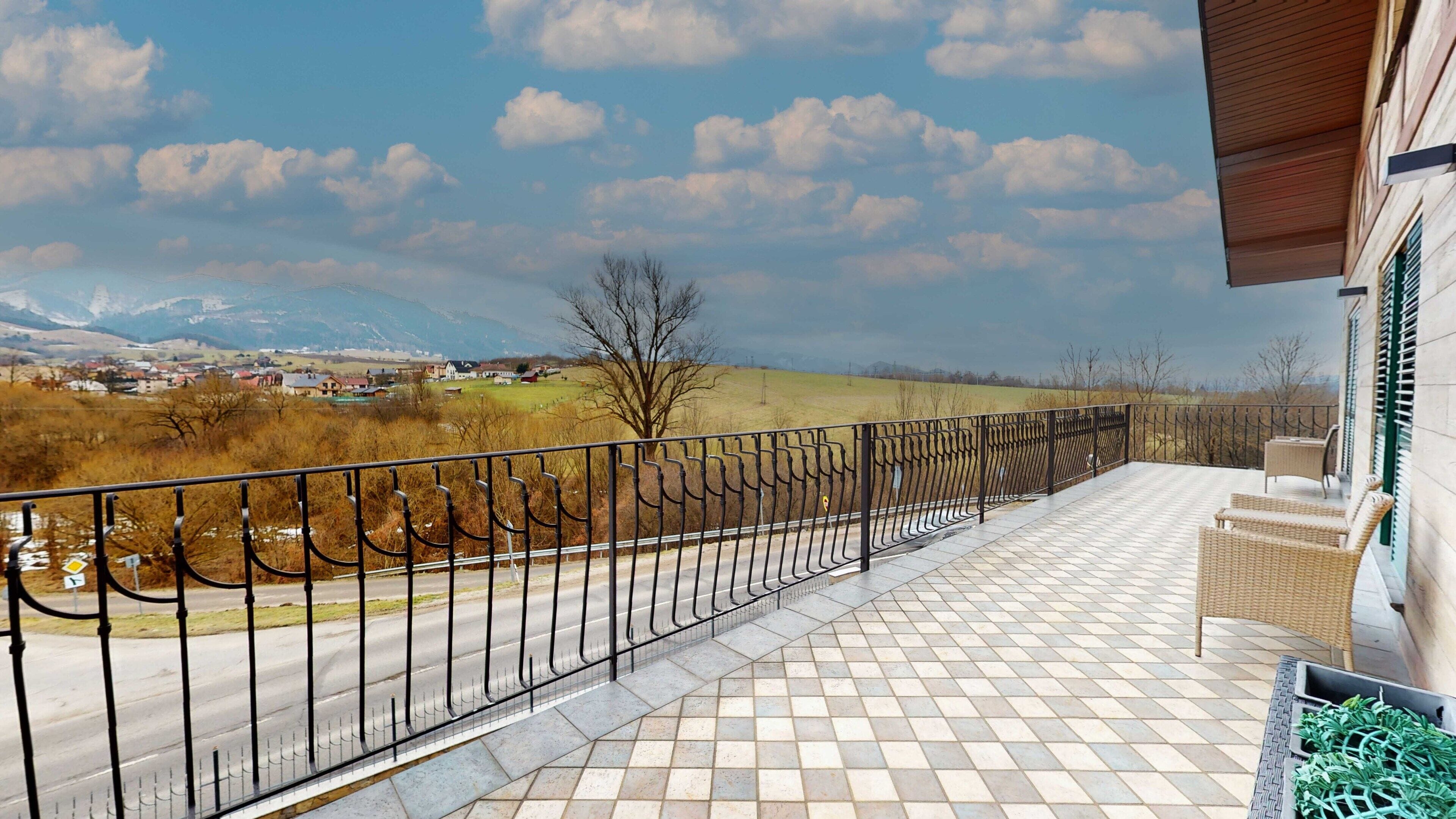 A balcony with a tiled floor and a metal railing overlooking a road and distant landscape.