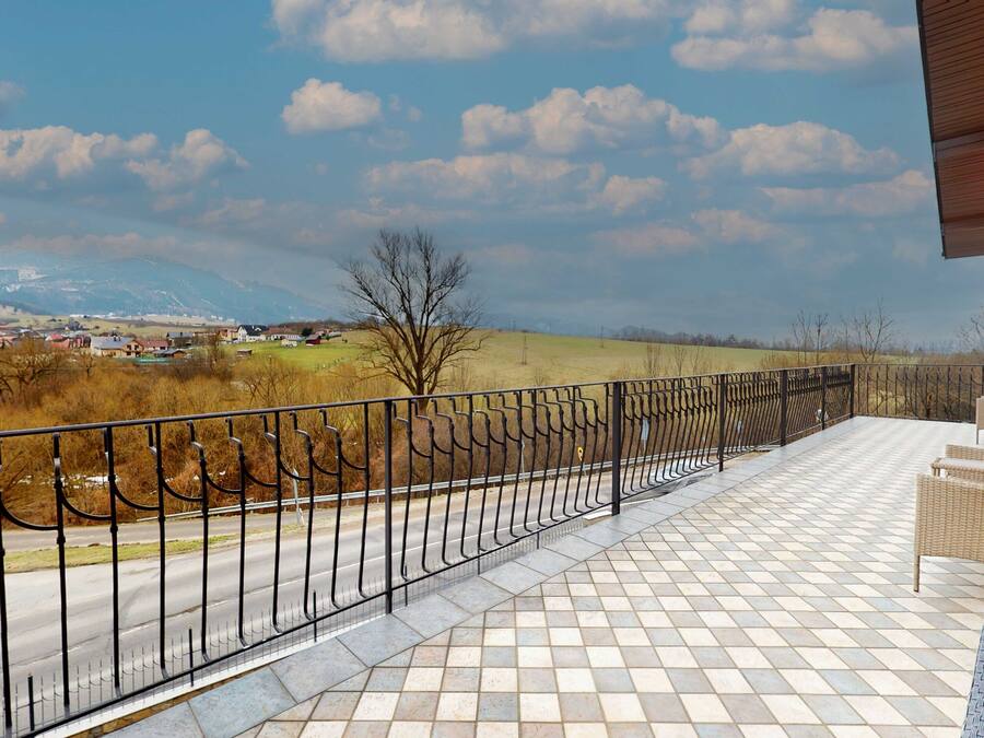 A balcony with a tiled floor and a metal railing overlooking a road and distant landscape.