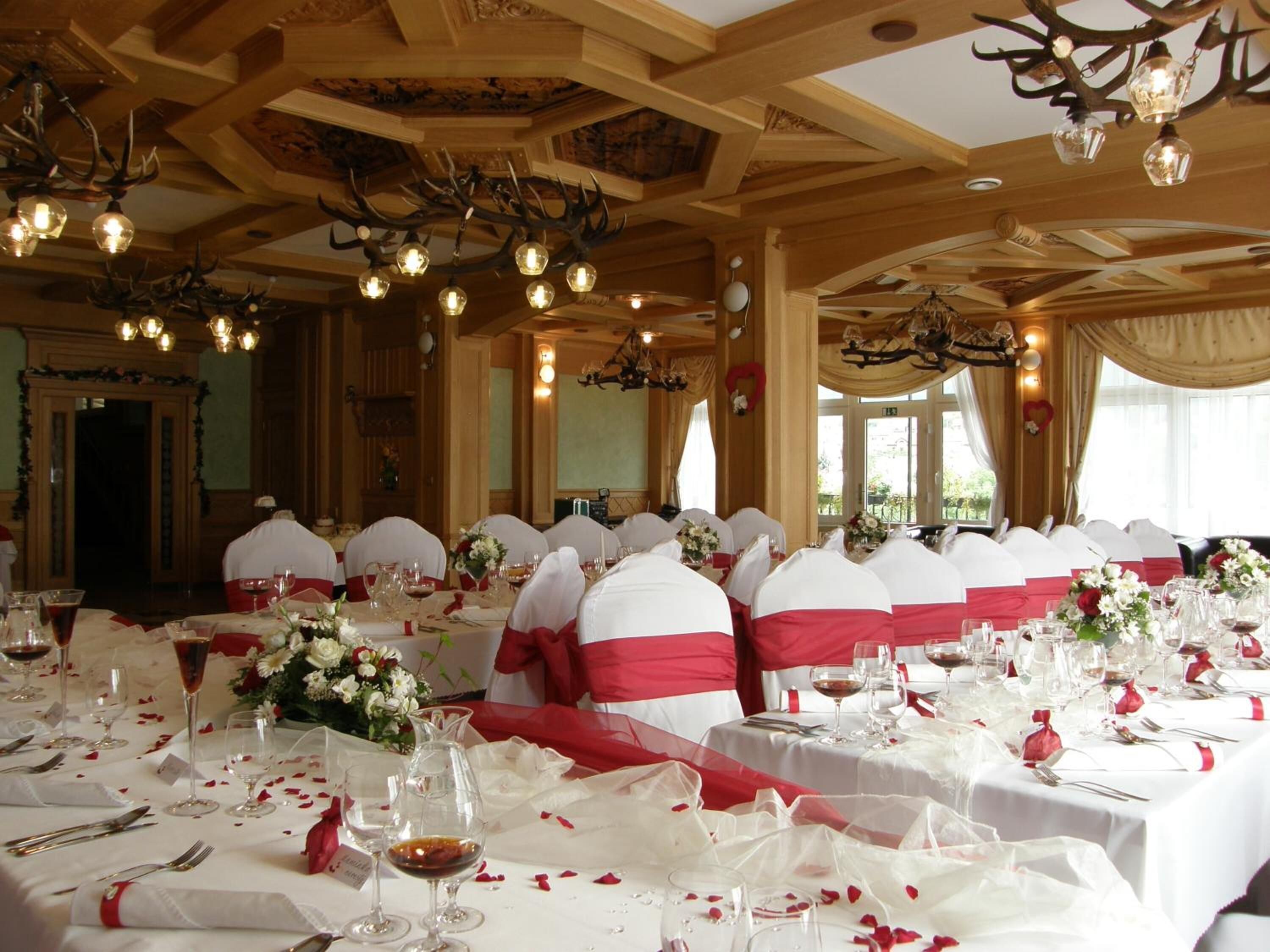 A banquet hall with round tables set for a formal event, featuring white tablecloths, red sashes, and floral centerpieces.