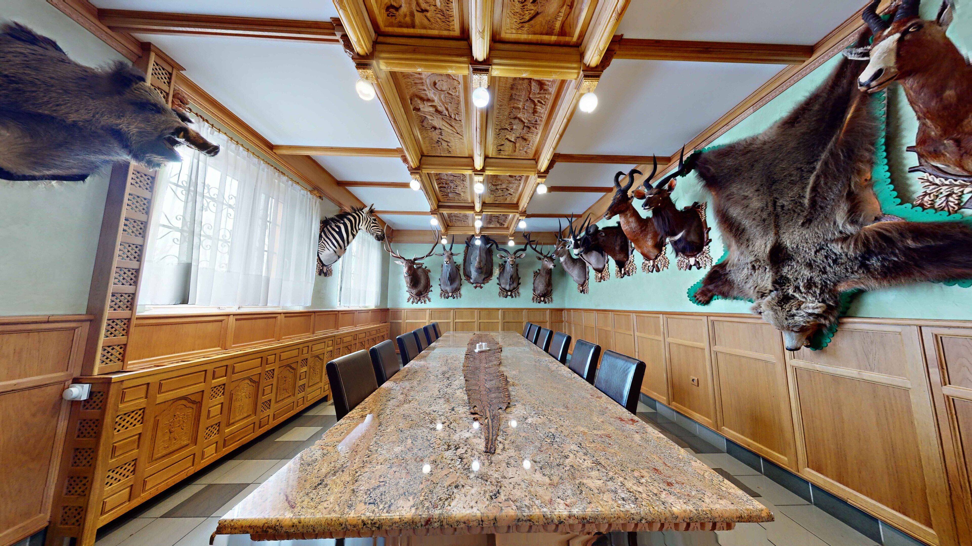 A dining room with a long table, wooden paneling, and mounted animal heads on the walls.