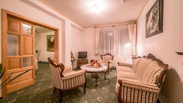 A living room with a green patterned carpet, a wooden door, a television, a sofa, and a framed picture on the wall.
