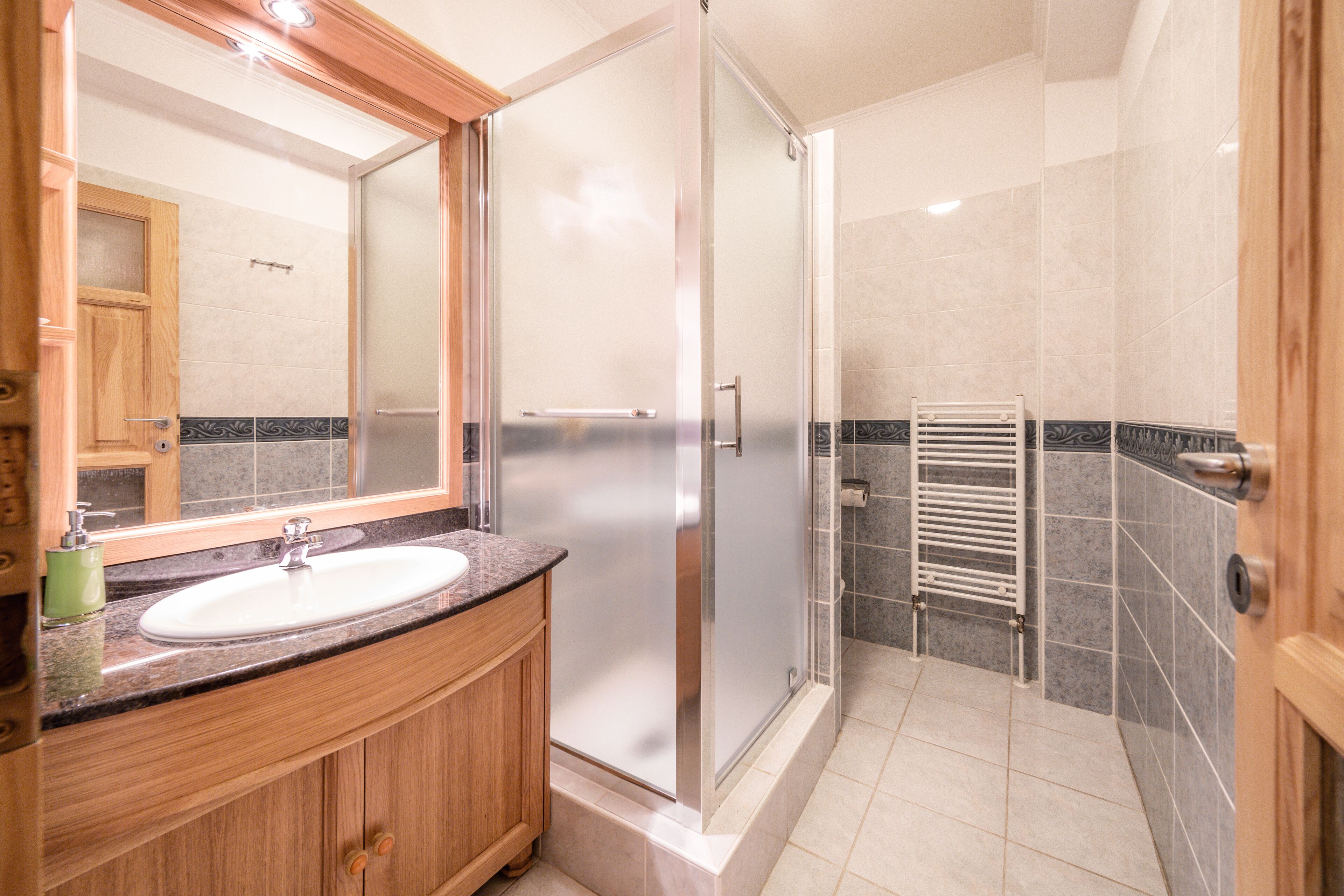 A modern bathroom with a wooden vanity, a large mirror, a glass shower enclosure, and a towel rack.